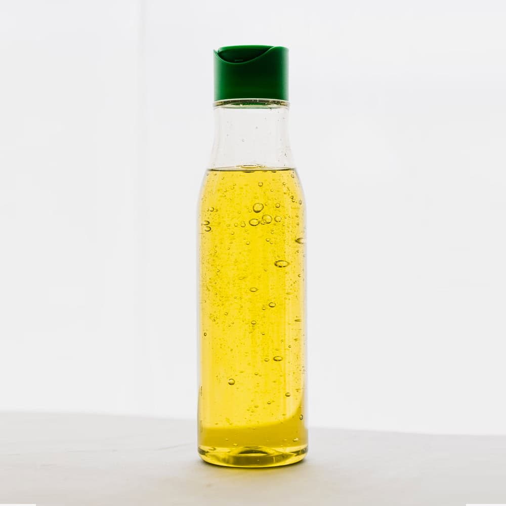 Thin glass bottle of yellow cooking oil with green cap on white background.
