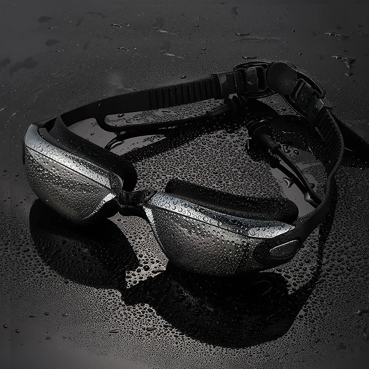 Anti-fog prescription swimming goggles with UV protection and integrated earplugs covered in water droplets on a dark reflective surface